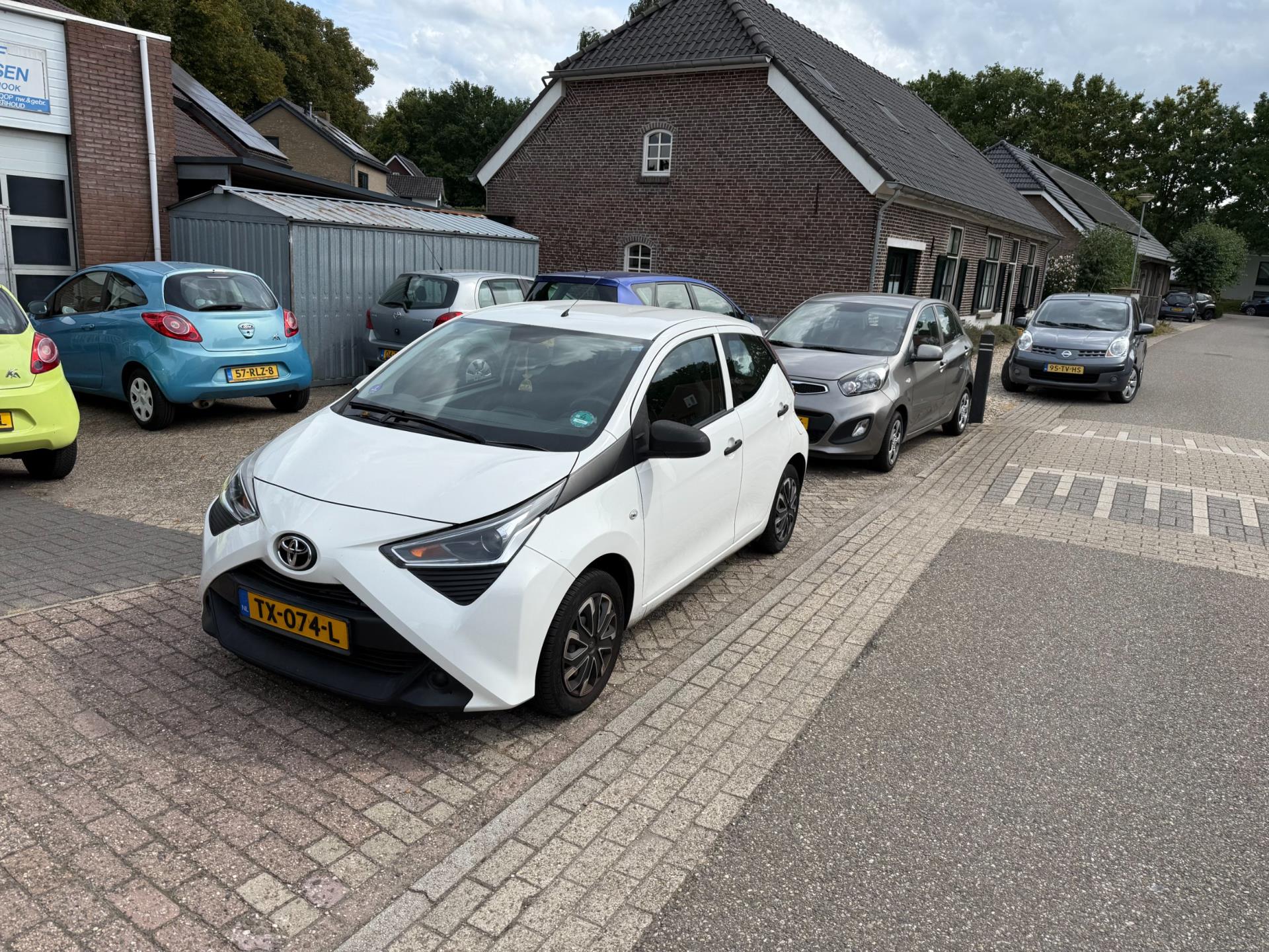 Een witte Toyota Aygo op het terrein van Autobedrijf Thijssen, met links boven de naam op het pand