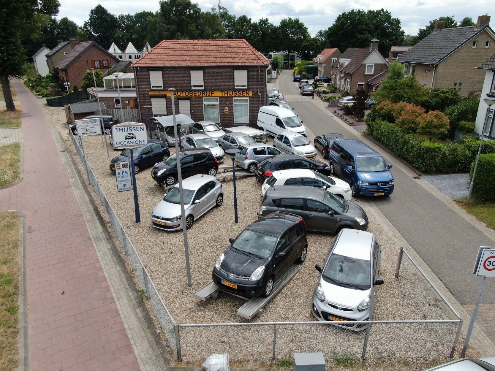 Het pand van Autobedrijf Thijssen met de naam op de gevel en het terrein vol occasions aan de Rijksweg in Mook, gezien van boven